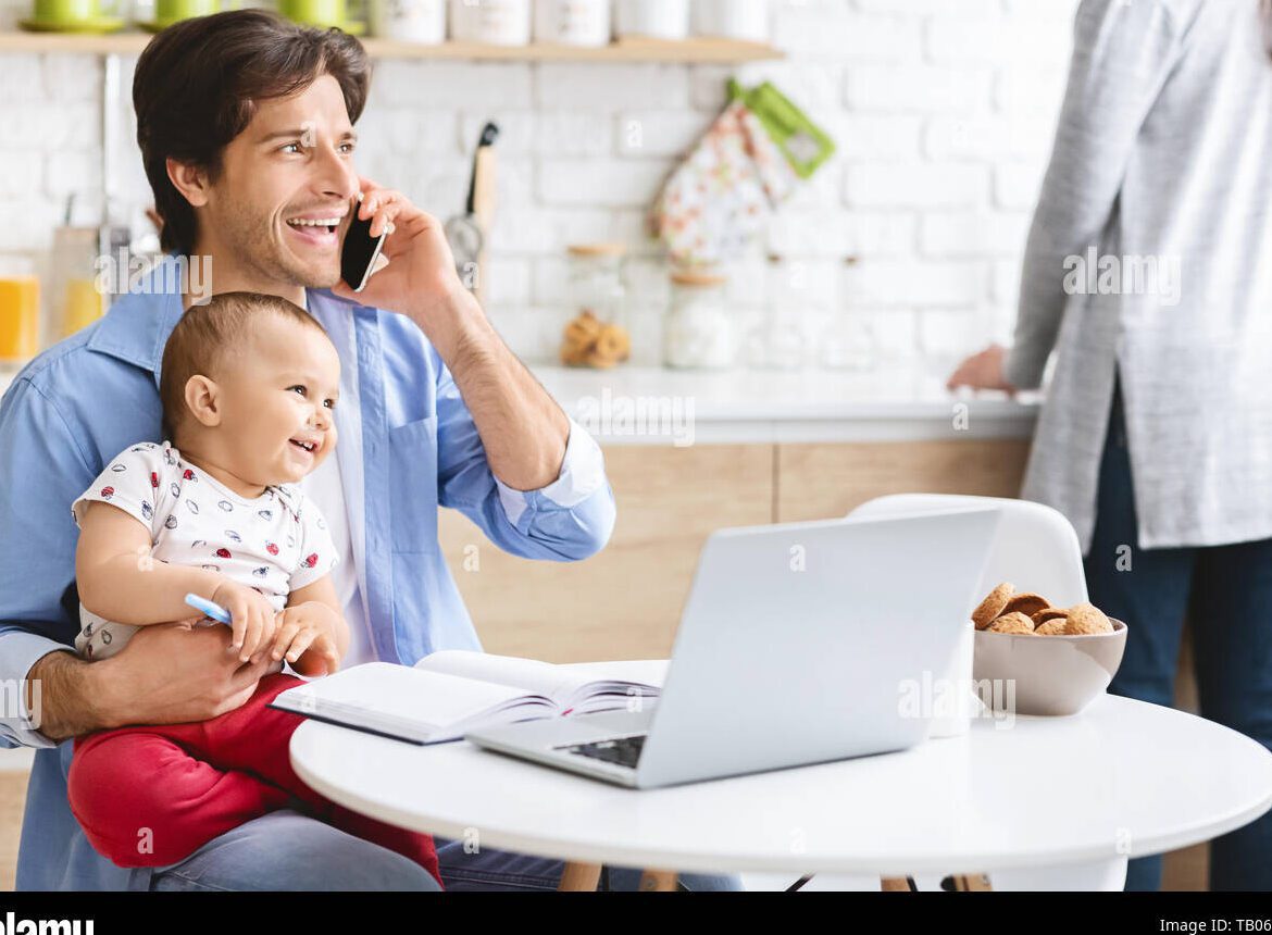 father holding baby while working from home